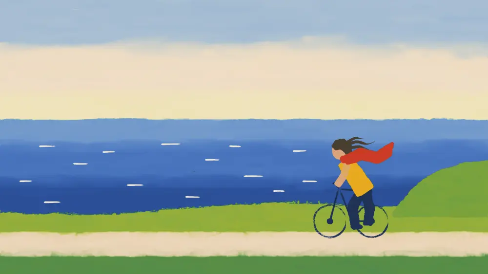 A woman cycling along a coast road, her red scarf flying.