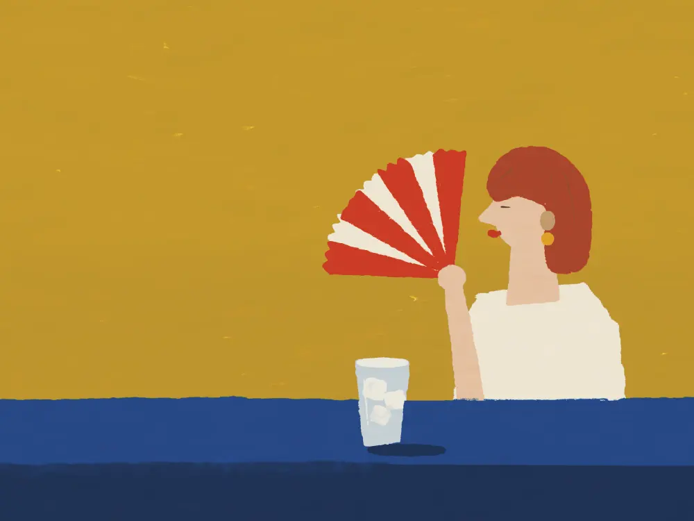 A woman with an auburn bob fanning herself at a café table, a glass of iced water beside her.