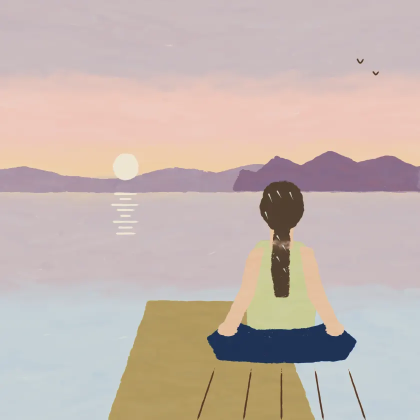 A woman with a long brown plait sitting cross-legged on a jetty at dawn.